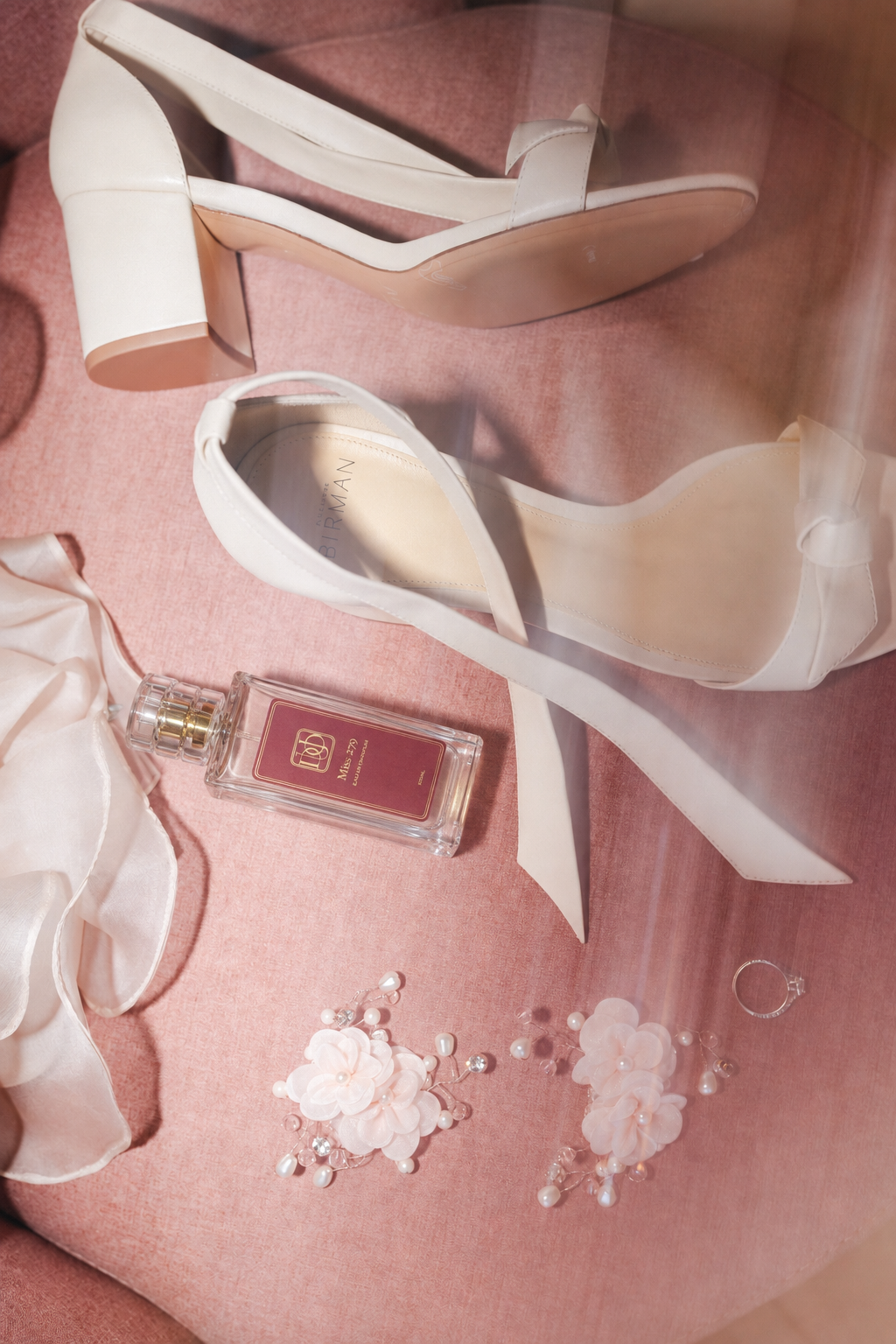 Perfume Miss 279 entre sapatos de noiva e acessórios sobre tecido rosa, com luz suave.