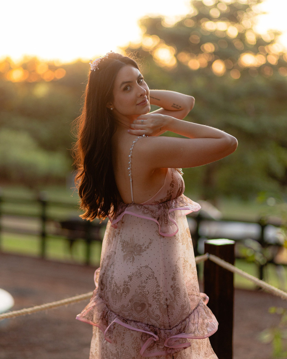Caroline Duó com as mãos junto ao pescoço, iluminada pelo pôr do sol.