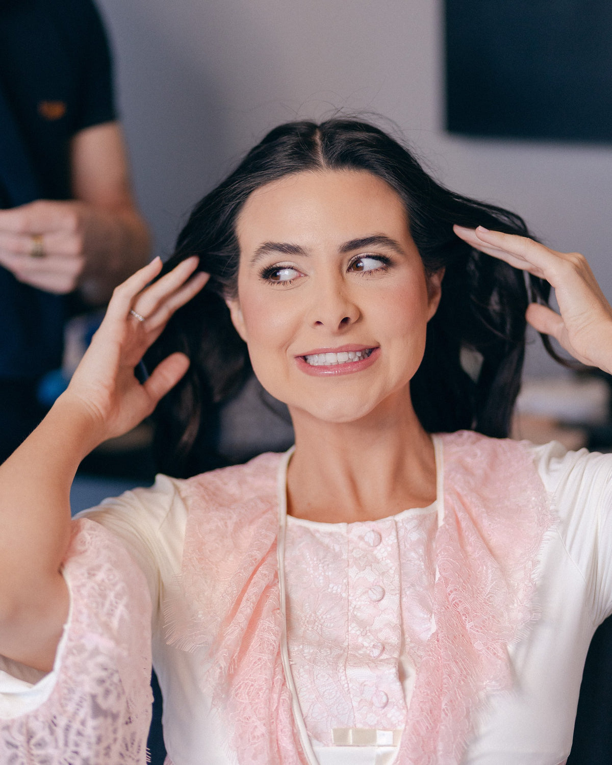 Caroline Duó sorrindo, com robe rosa e as mãos nos cabelos.