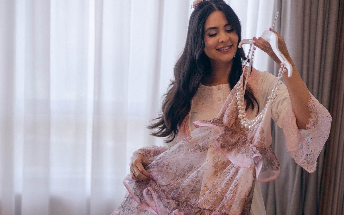 Caroline Duó segurando seu vestido rosa junto à janela.